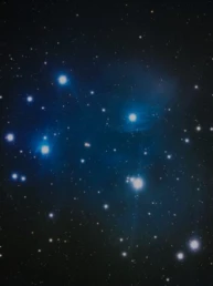 Pleiades star cluster (M45) astrophotography showing bright blue stars surrounded by faint reflection nebula in the Taurus constellation.