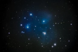 Pleiades star cluster (M45) astrophotography showing bright blue stars surrounded by faint reflection nebula in the Taurus constellation.